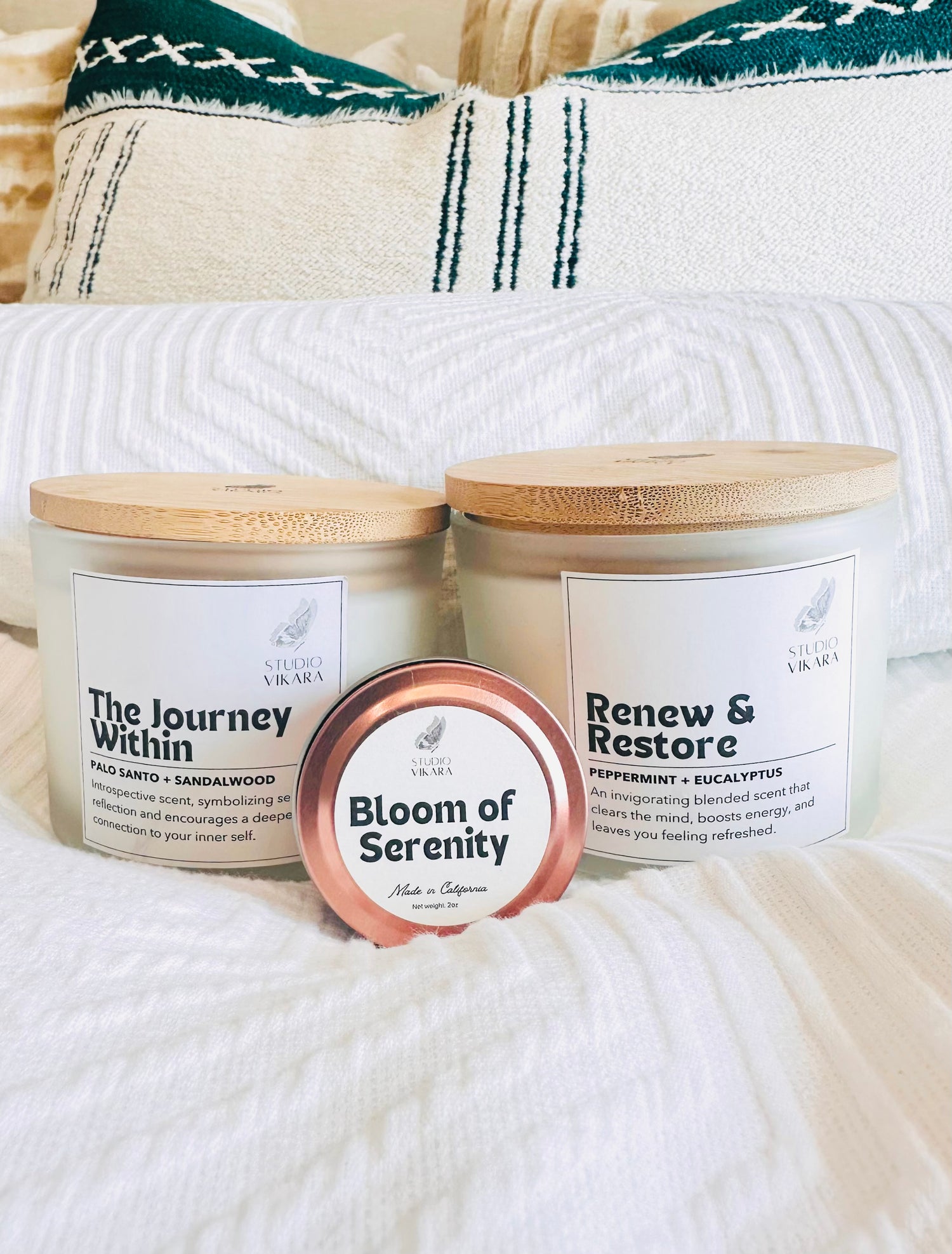 Two big jars of candle and a small rose gold tin candle arranged on a luxury bed